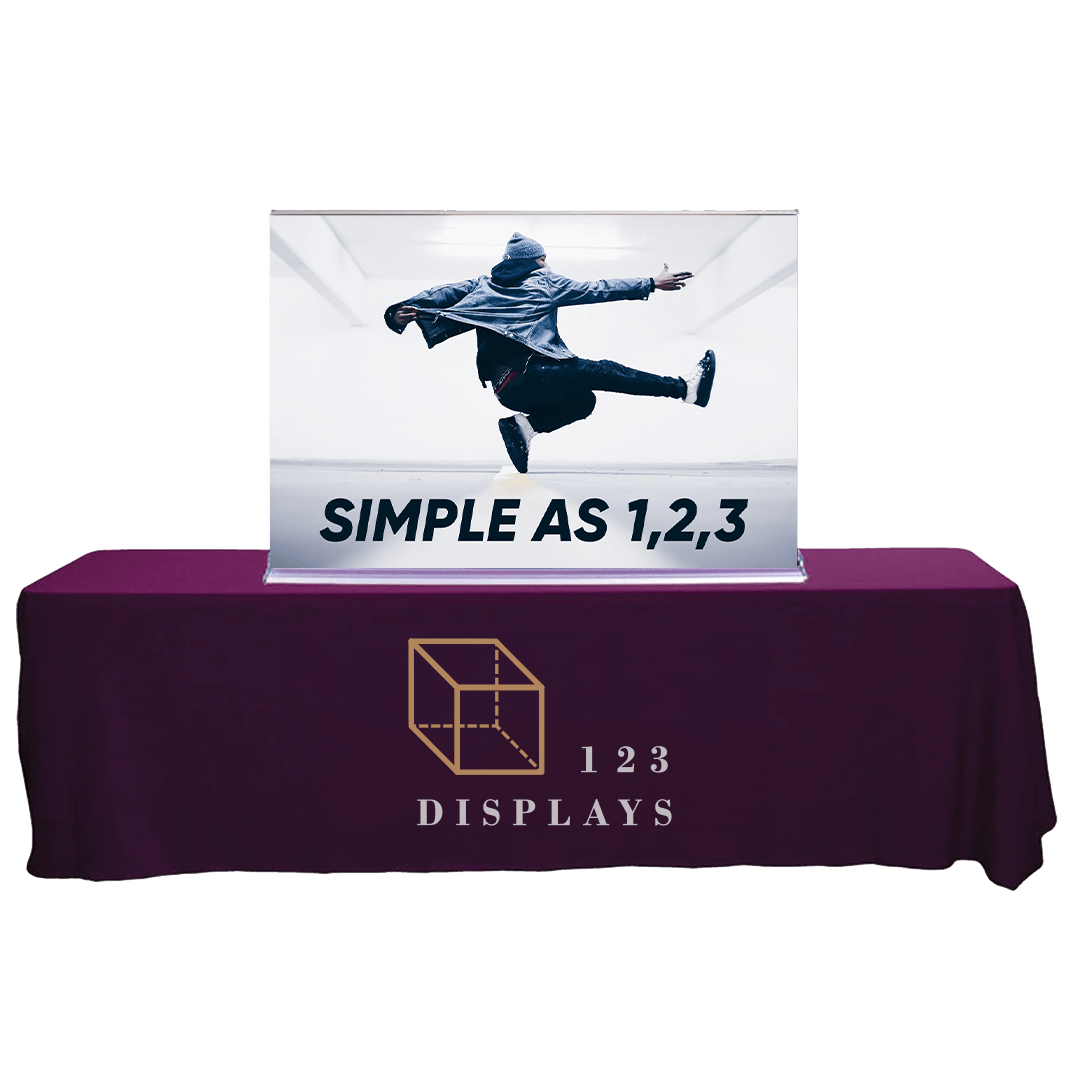 Promotional display for 123 Displays with a purple branded table cover, a lightbox featuring an energetic jumping figure photo, and a banner showing the company's logo, name and 'SIMPLE AS 1,2,3' slogan.